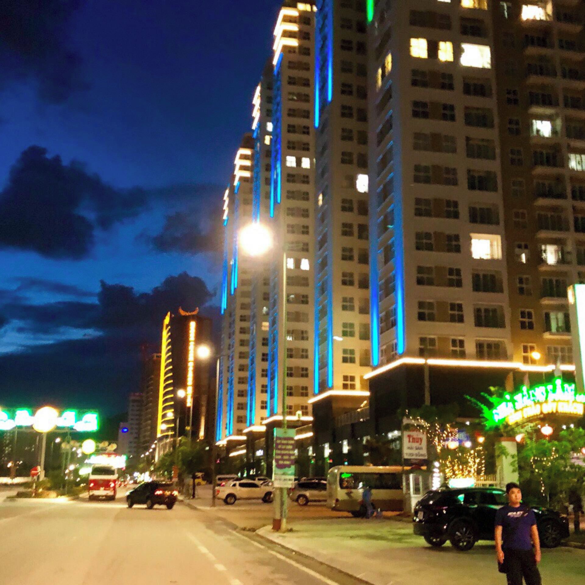Una calle urbana iluminada de noche, con edificios altos, farolas y vehículos.