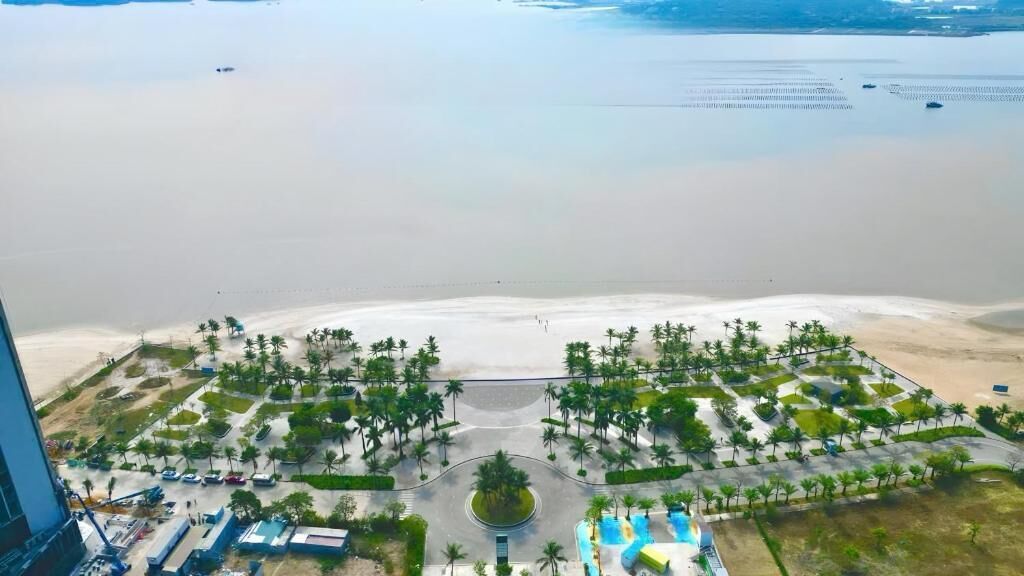 An aerial view of a resort with a beach, palm trees, and a central roundabout.