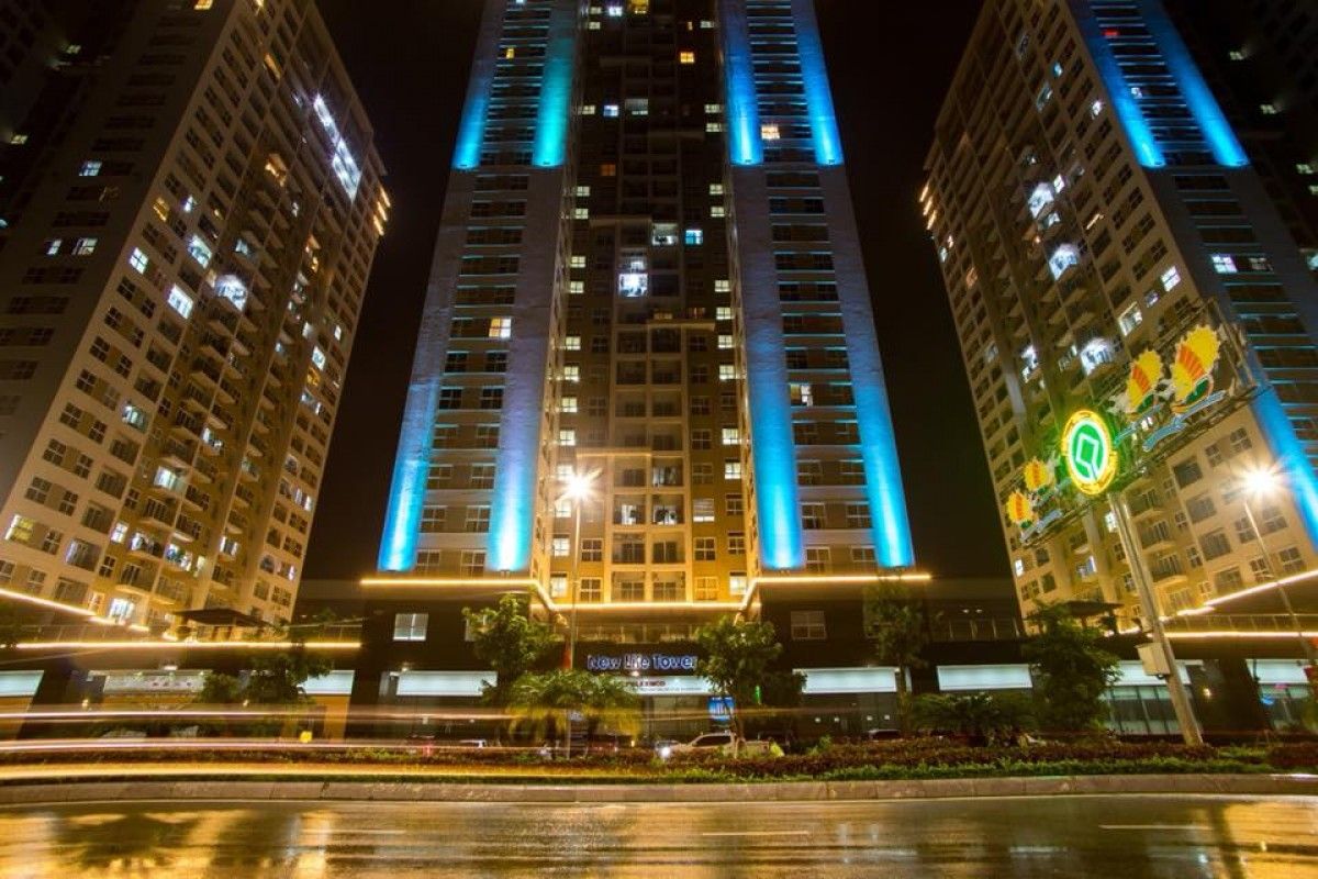 Un hotel de gran altura con líneas verticales iluminadas en la fachada, una entrada central y un letrero que dice "New Life Tower".