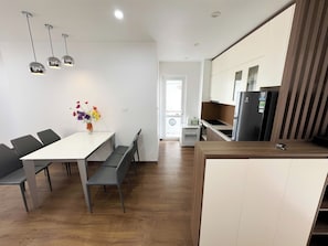 A modern kitchen with a central island, a dining area with a white table and grey chairs, and pendant lighting. - New Life Tower Bai Chay (Bai Chay)