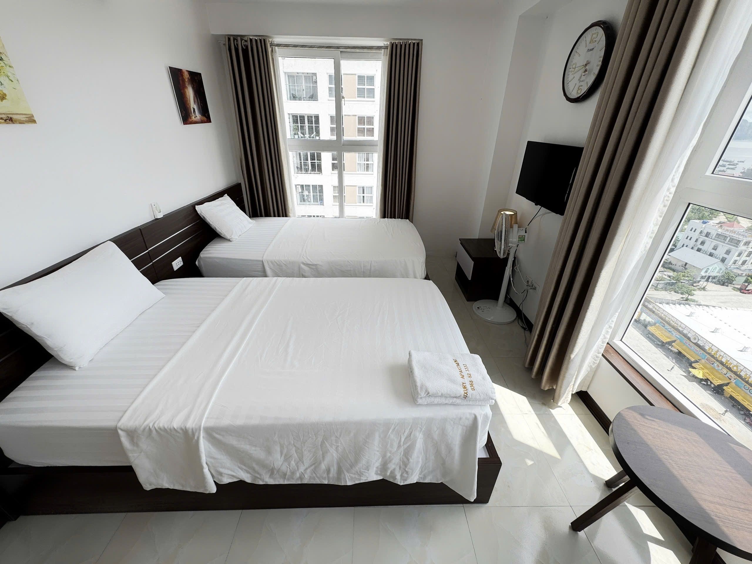 Habitación de hotel con dos camas, una mesita de noche, un televisor y una ventana con cortinas.