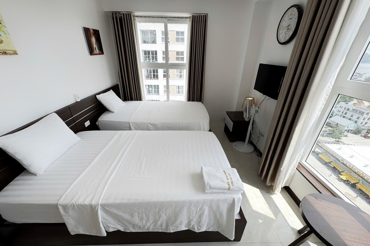 A hotel room with two beds, a bedside table, a TV, and a window with curtains.