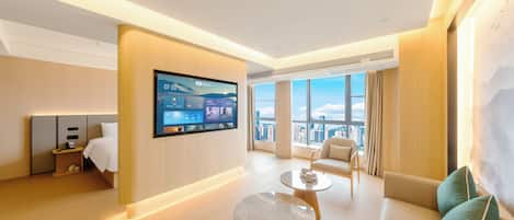 Una habitación de hotel moderna con un televisor grande montado en la pared, un sofá, una mesita de centro y vistas a la ciudad a través de amplios ventanales.