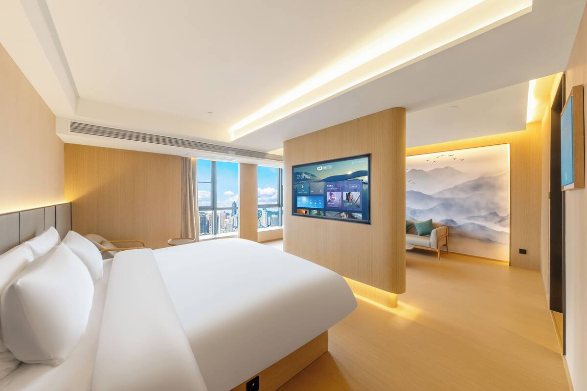 Une chambre d’hôtel moderne avec un grand lit, un téléviseur fixé au mur et une vue sur la ville.
