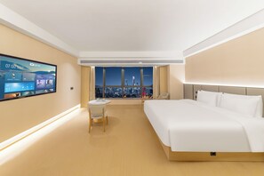 Hotellihuone, jossa on suuri sänky, työpöytä, tuoli, televisio ja suuri ikkuna, josta avautuu näkymä kaupungin ylle.