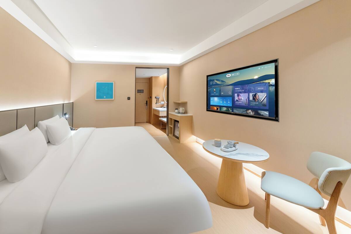 Une chambre d’hôtel moderne avec un grand lit, un téléviseur fixé au mur, une petite table ronde et deux chaises.