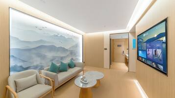 A modern hotel room with a large wall mural, a sofa with cushions, a round coffee table, and a mounted TV screen.