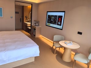 A hotel room with a large bed, a desk with a chair, a small table with cups, and a TV displaying a program. - Xianze Hotel (Guangzhou)