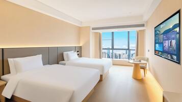 A hotel room with two beds, a large window with a city view, a round table, and a mounted TV.