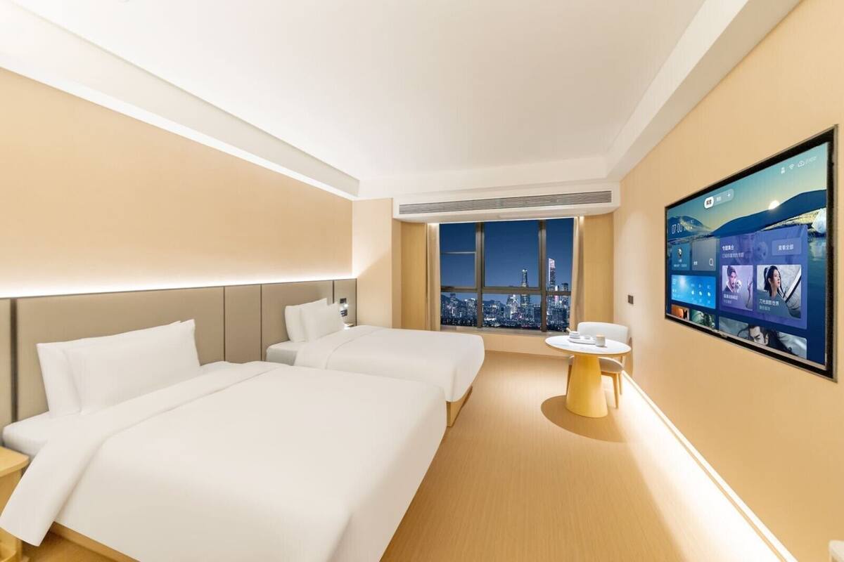 Une chambre d’hôtel avec deux lits, une petite table et un grand écran de télévision qui diffuse une vue panoramique sur la ville.