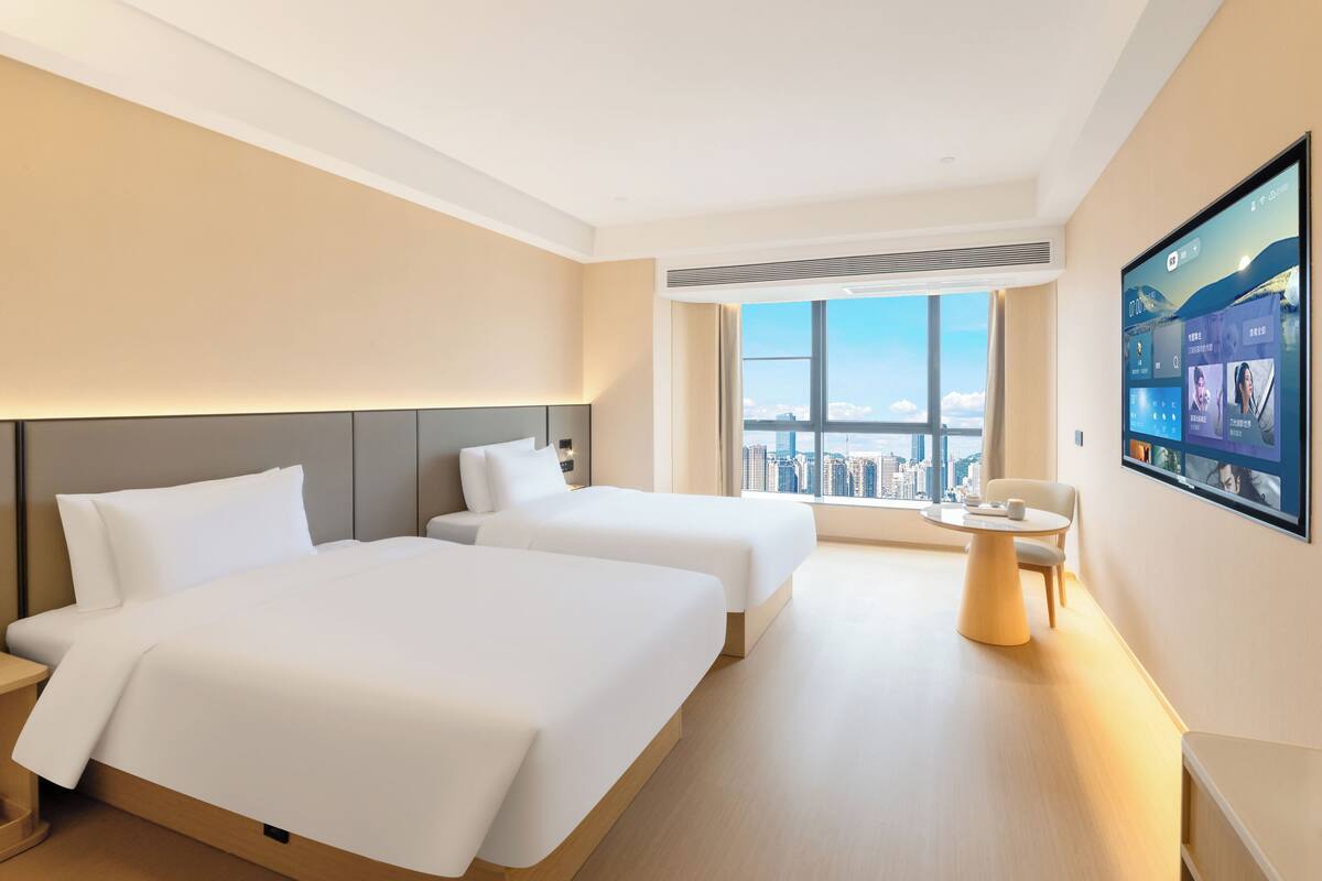 Une chambre d’hôtel avec deux lits, une grande fenêtre donnant sur la ville, une table ronde et un téléviseur fixé au mur.