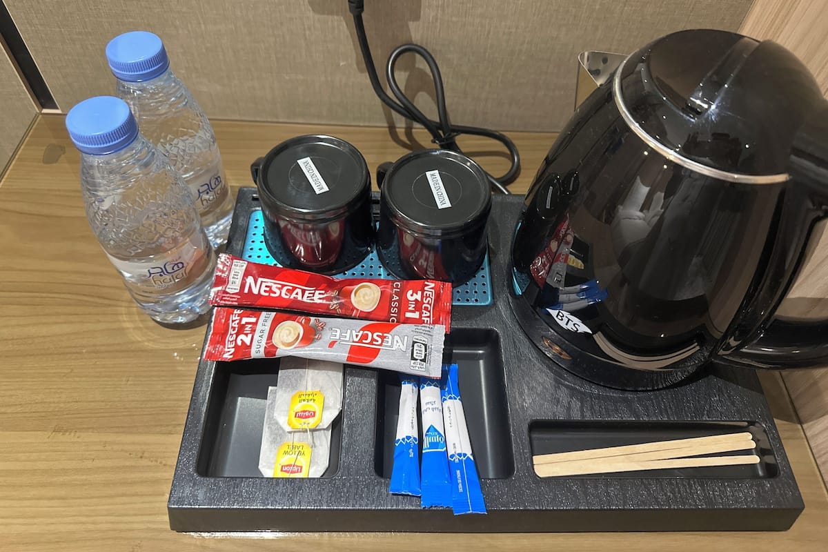 Une machine à café, deux bouteilles d’eau, un paquet de café Nescafe, un paquet de thé et des baguettes, le tout sur un plateau.