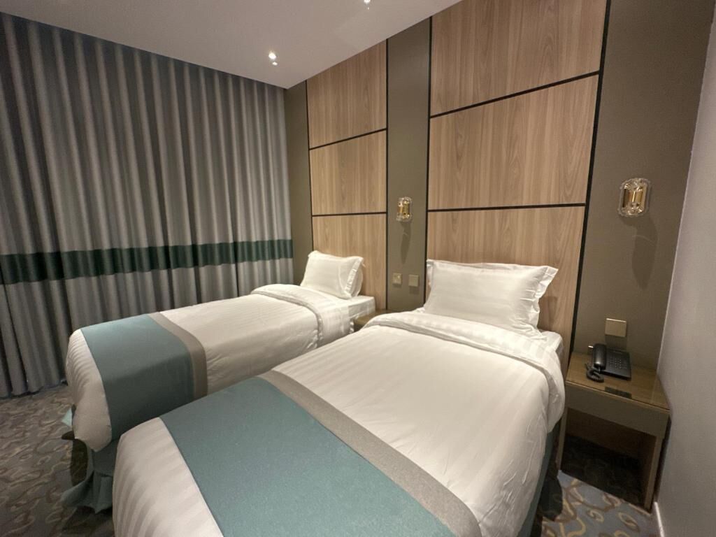 A hotel room with two beds, a wooden headboard, a desk with a phone, and a curtain.