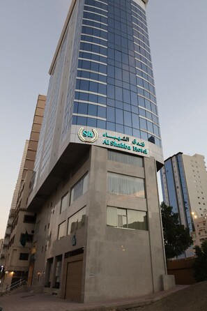 Un moderno edificio de hotel con fachada de vidrio y un letrero que indica que es el Hotel AlShahba.