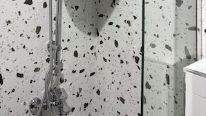 Ducha con diseño moderno, cerramiento de vidrio y suelo de terrazo.