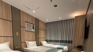 Habitación de hotel con dos camas, televisión, un cesto de basura y alfombra estampada.