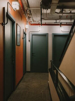 Un pasillo con tres puertas, cada una con un número. Las paredes están pintadas en dos colores y el suelo tiene una alfombra estampada.