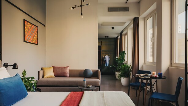 A hotel room with a bed, a sofa, a small table, a chair, a potted plant, and a window with curtains. - Brassbell Dt Hannaux Tahrir Sq (Cairo)