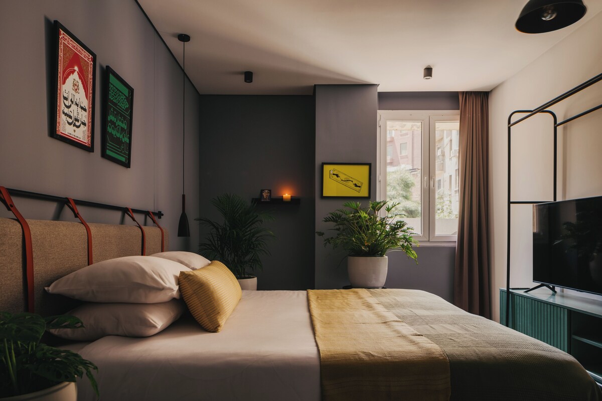 A modern bedroom with a bed, potted plants, and artwork on the walls.