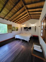 Una habitación con techo de madera, una cama con cubrecama blanco, un banco y obras de arte en las paredes.