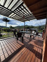 Una terraza de madera con mobiliario exterior, un espacio cubierto y vistas a un paisaje montañoso.