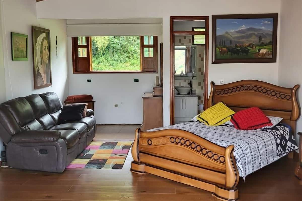 Un dormitorio con cama de madera, sofá de cuero, baño pequeño y vistas a zonas verdes.