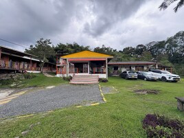 A small building with a yellow roof, a porch, and a staircase leading to the entrance. There are cars parked in front and a grassy area with a paved path leading to the building.