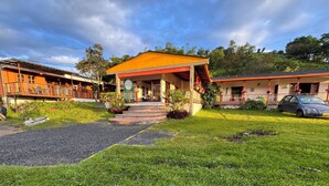 A building with a red roof and a porch, surrounded by a well-maintained lawn and a gravel path leading to the entrance. - Kumanday Lodge  (Pereira)