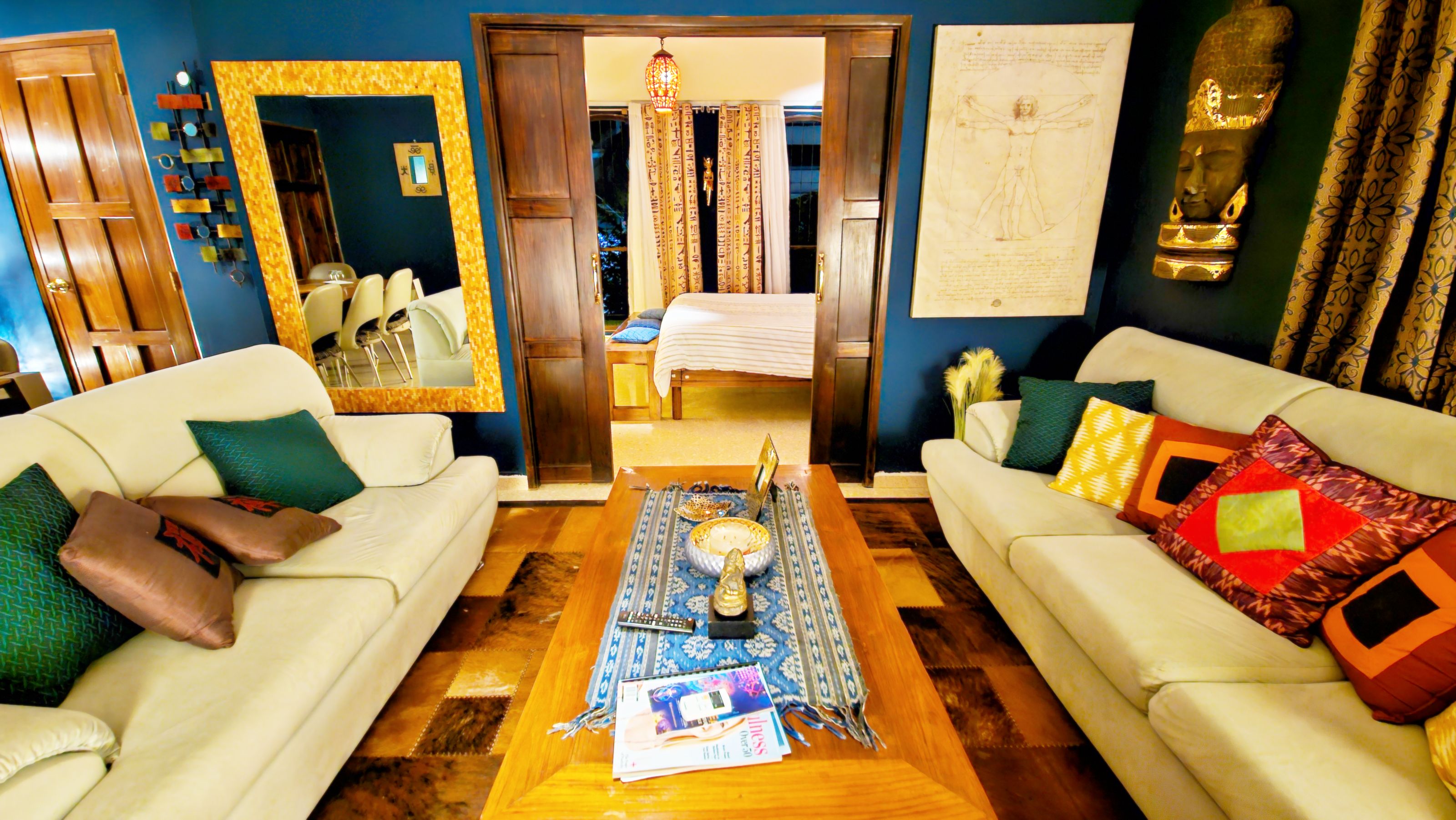 A living room with two sofas, a coffee table, a mirror, a bed with curtains, and a wall with a framed drawing.