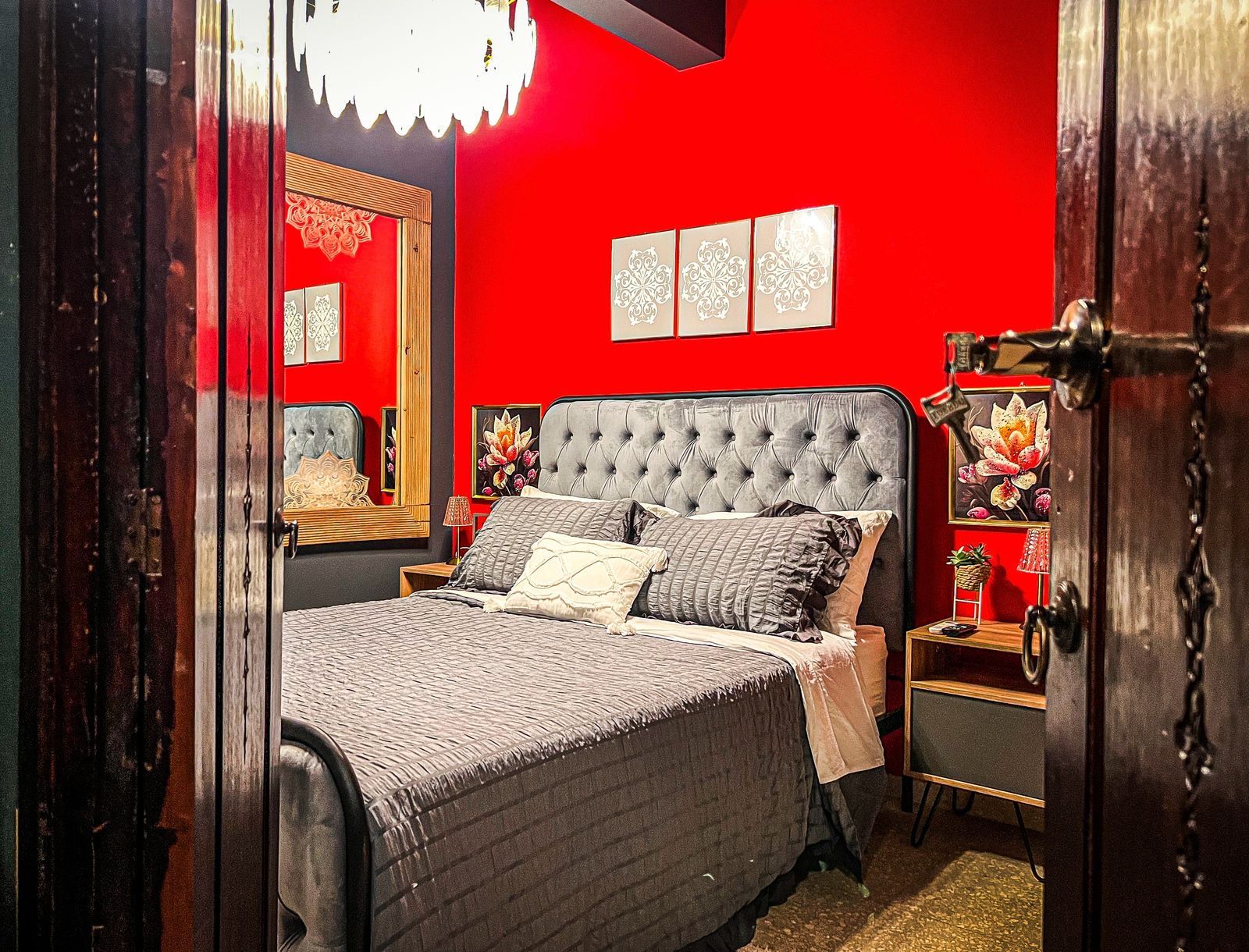 A bedroom with a tufted headboard, a bed with multiple pillows, a nightstand, and a mirror.
