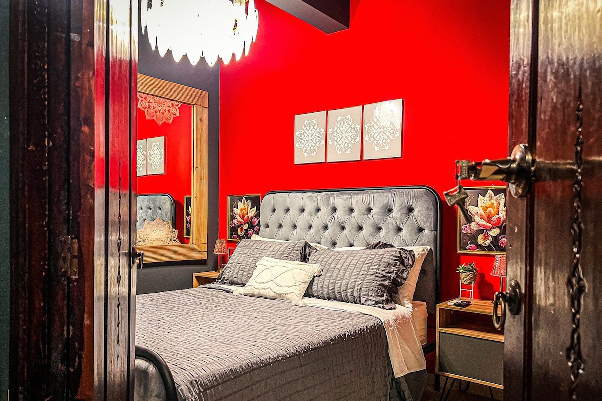 Ein Schlafzimmer mit einer gepolsterten Kopfteile, einem Bett mit vielen Kissen, einem Nachttisch und einem Spiegel.