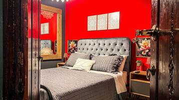 A bedroom with a tufted headboard, a bed with multiple pillows, a nightstand, and a mirror.
