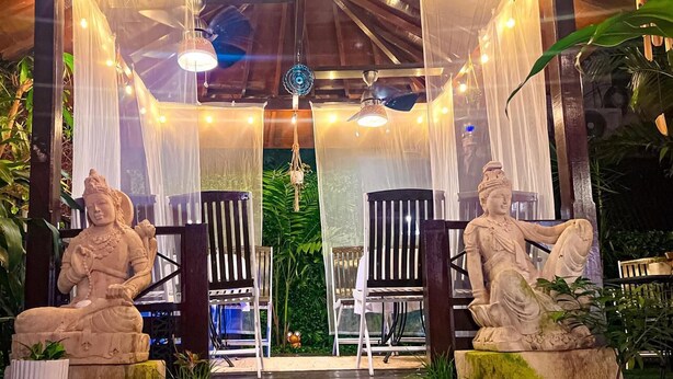 Un espace extérieur paisible, aménagé avec deux statues en pierre, des chaises en bois et un auvent.