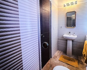 Une salle de bain avec un mur à motifs, une porte noire, un lavabo et un miroir.