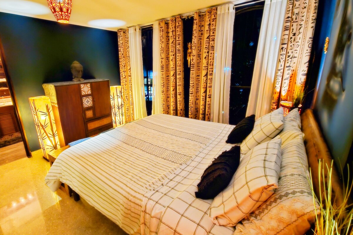 Une chambre d’hôtel avec un grand lit, une salle de bain avec un miroir et une vue sur la ville la nuit, vue depuis la fenêtre.