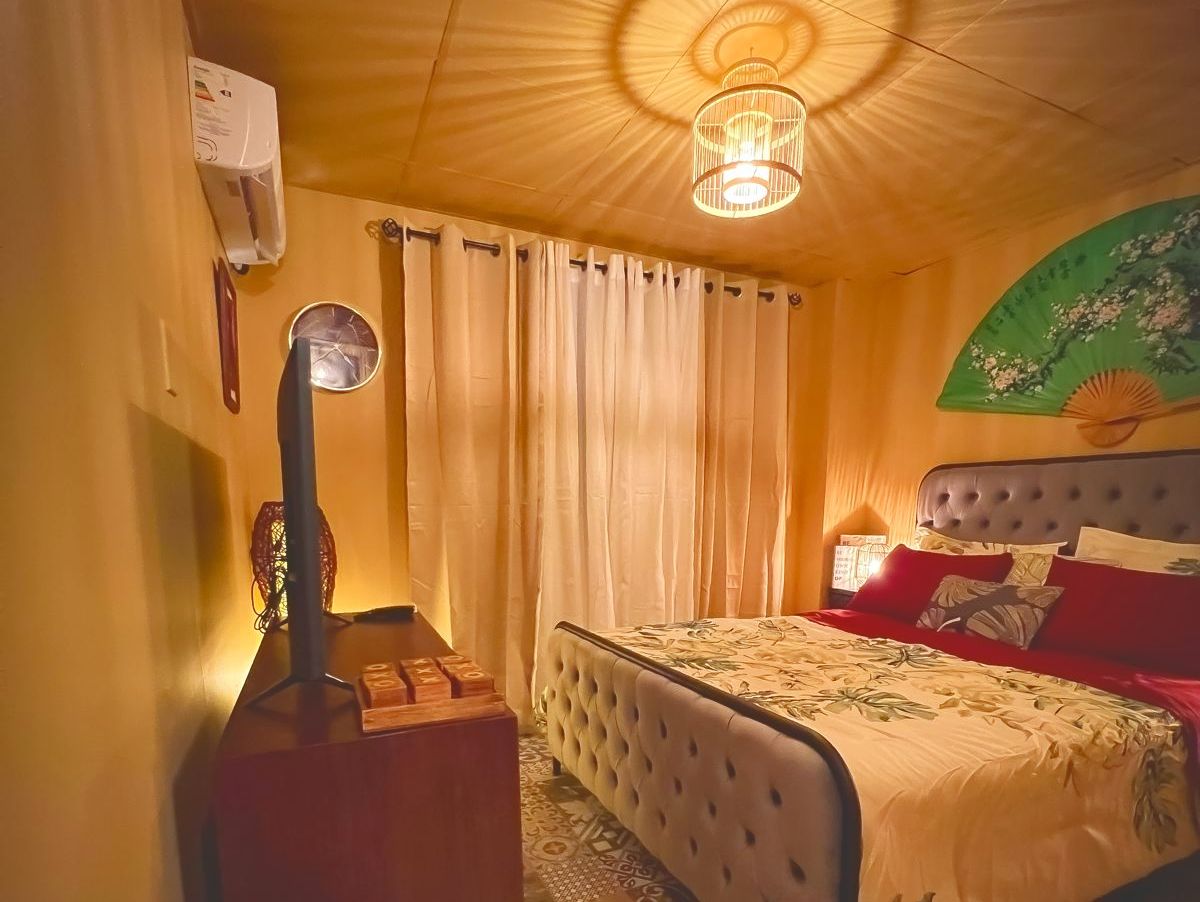 Een slaapkamer met een bed, gordijnen, een lamp en een wandairconditioner.