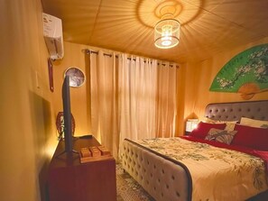 Ein Schlafzimmer mit einem Bett, Vorhängen, einer Lampe und einer Wandklimaanlage.