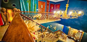 Un intérieur à plusieurs niveaux, agrémenté d’un escalier en bois, de lustres et d’objets décoratifs.