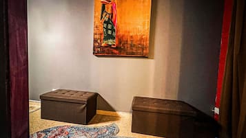 Una stanza con un quadro appeso al muro, due pouf scuri e un tappeto decorato sul pavimento.