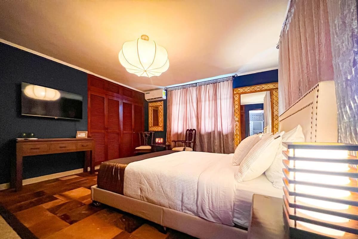 Un dormitorio con cama, mesita de noche y televisor sobre un mueble.