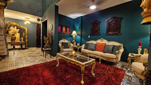 Un salon luxueux, agrémenté de meubles richement décorés, d’un tapis rouge et d’œuvres d’art ornementales accrochées aux murs.