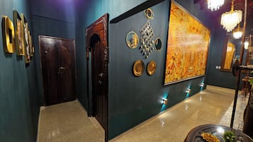 Een hal met een donkere houten deur, een grote sierlijke spiegel en een wand met een groot decoratief schilderij.