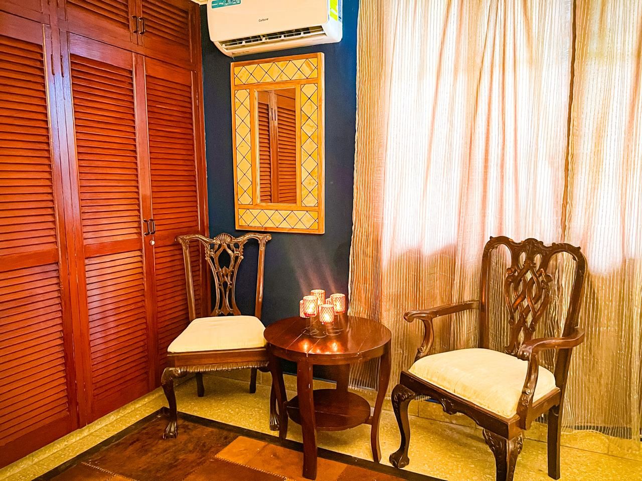A room with a wooden wardrobe, a table with chairs, a wall-mounted air conditioner, and a window with curtains.