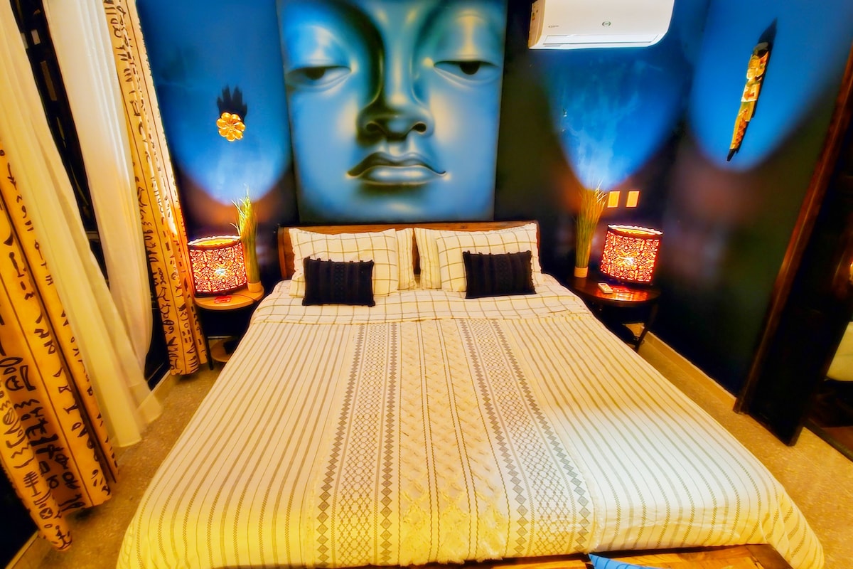 Une chambre d’hôtel avec un grand lit, deux tables de chevet, un climatiseur fixé au mur et un élément décoratif mural.