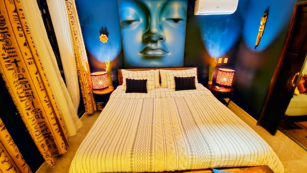 Une chambre d’hôtel avec un grand lit, deux tables de chevet, un climatiseur fixé au mur et un élément décoratif mural.