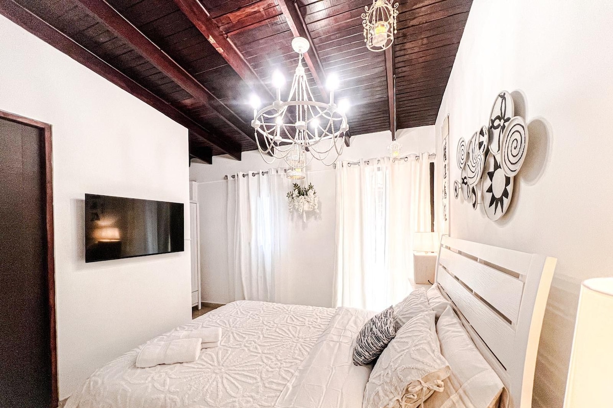 Ein Schlafzimmer mit einem Bett, einer Kandelaber, einem Flachbildfernseher und Wandbildern.