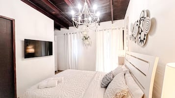 A bedroom with a bed, a chandelier, a flat-screen TV, and wall art.