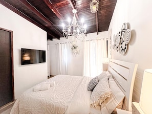 A bedroom with a bed, a chandelier, a flat-screen TV, and wall art. - Orho Hotel Boutique 15 Minutes From PTY Airport (Tocumen)