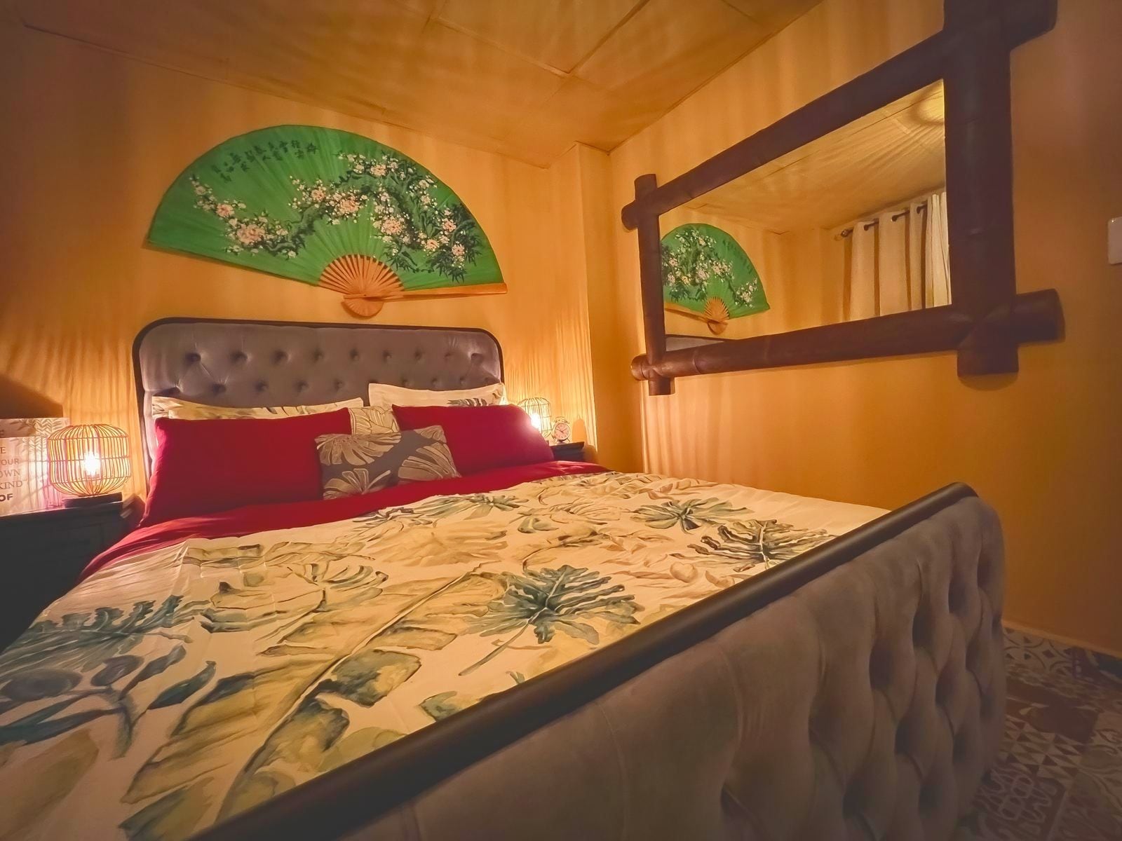 A bed with a floral bedspread, a green fan with floral patterns, and a mirror with a floral design.