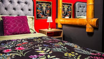 Una cama con colcha floral, cabecera capitonada y mesita de noche con lámpara.